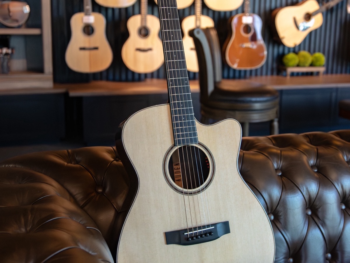 Auden acoustic guitar resting on a leather couch in the Corzic Music showroom